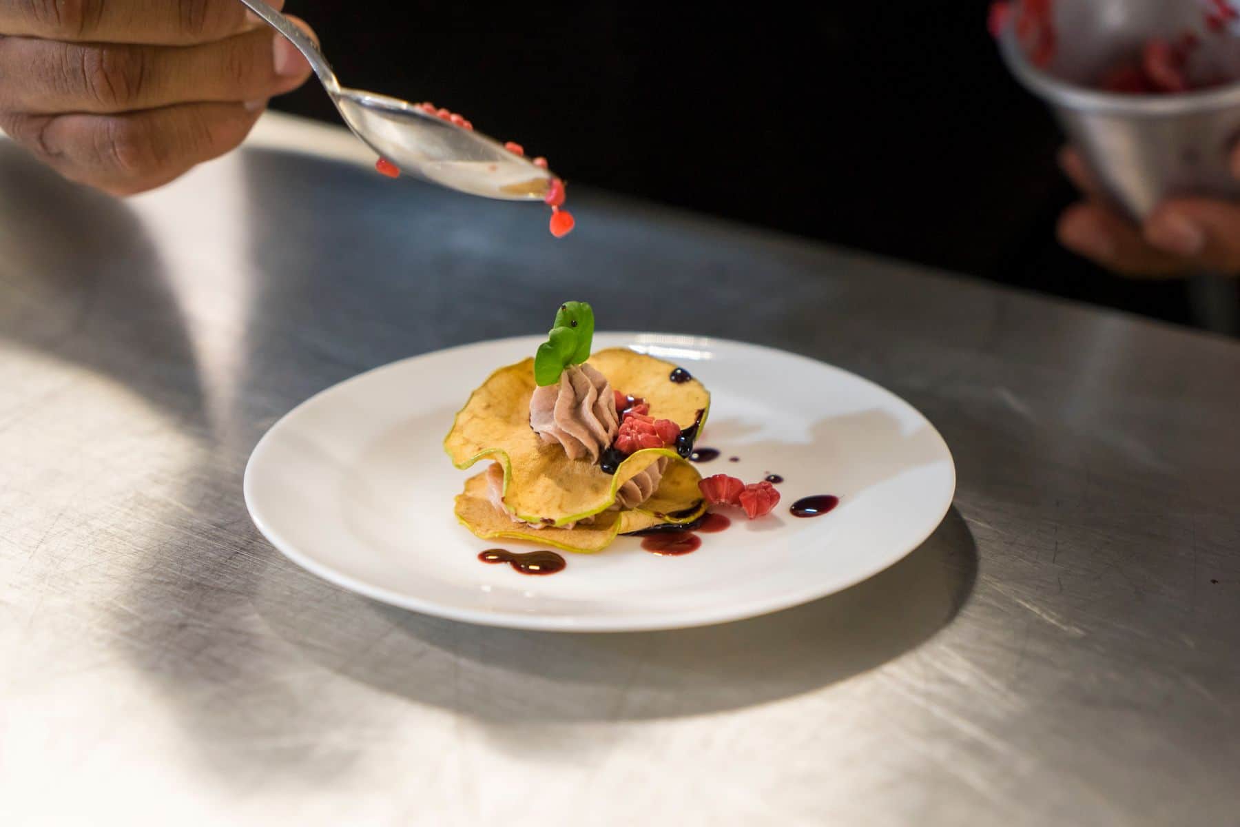 A chef finishing a plate on the kitchen pass