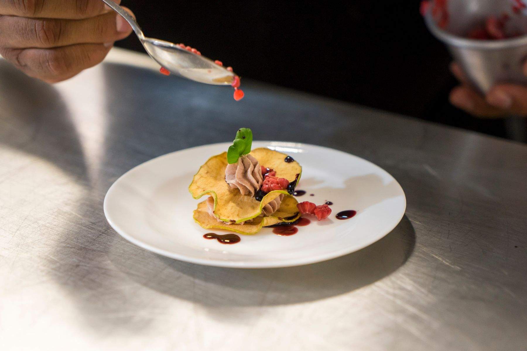 A chef finishing a plate on the kitchen pass